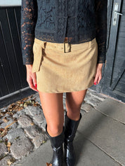Person wearing a beige skirt and black boots on a sidewalk.