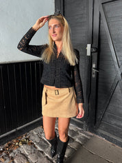 Woman in black lace top and beige skirt standing outside a building.